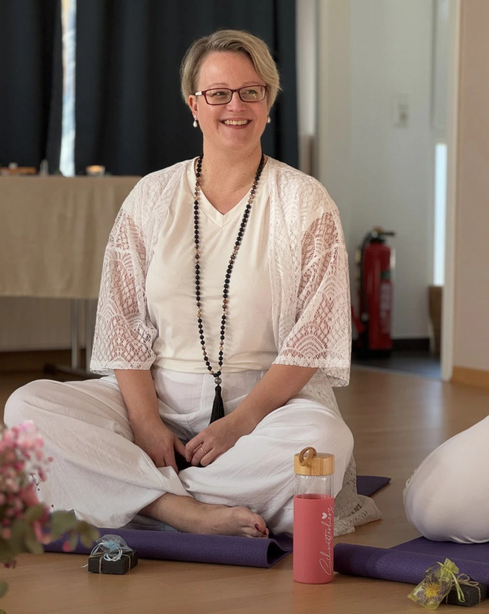 Frau in weißer Kleidung sitzt meditierend auf einer Yogamatte in einem hellen Raum für Achtsamkeit