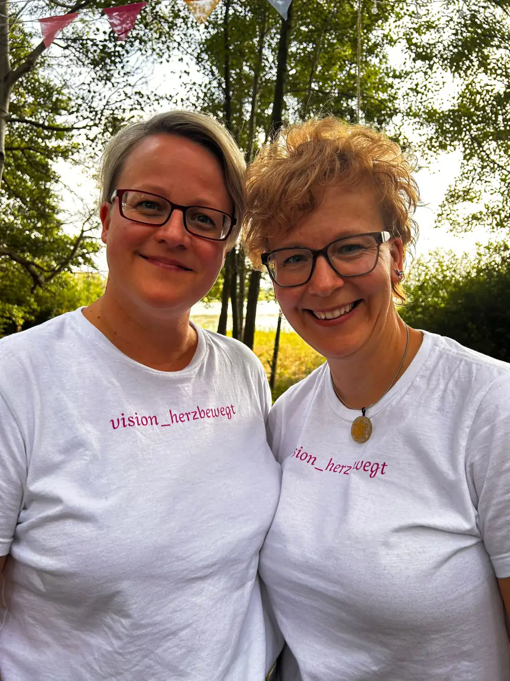 wei Frauen in weißen T Shirts mit "vision_herzbewegt" Aufdruck in einem Netzwerk für ganzheitliche Gesundheit.